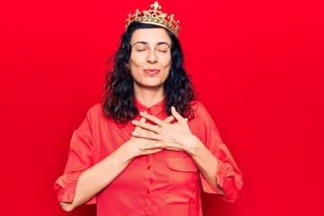 Young beautiful hispanic woman wearing princess crown smiling with hands on chest, eyes closed with grateful gesture on face. health concept.