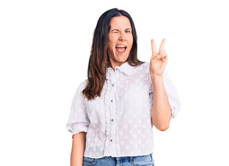 Young beautiful brunette woman wearing casual shirt smiling with happy face winking at the camera doing victory sign. number two.