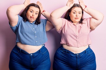 Young plus size twins wearing casual clothes doing bunny ears gesture with hands palms looking cynical and skeptical. easter rabbit concept.