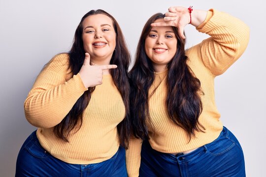 Young plus size twins wearing casual clothes smiling making frame with hands and fingers with happy face. creativity and photography concept.