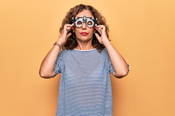 Middle age beautiful woman controlling vision using optometry glasses over yellow background with hand on head, headache because stress. Suffering migraine.