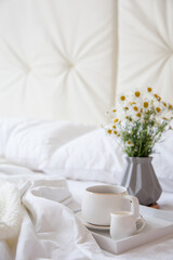 Cozy breakfast in bed, cup of coffee and milk on the grey fabric, space for text. Alarm clock for seven in the morning.