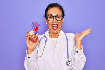 Middle age senior cardiologist doctor woman holding professional cardiology heart very happy and...