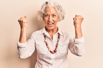 Obraz premium Senior grey-haired woman wearing casual clothes screaming proud, celebrating victory and success very excited with raised arms