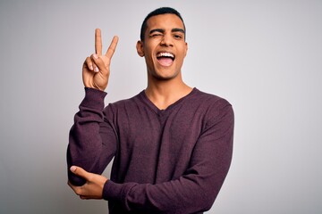Young handsome african american man wearing casual sweater over white background smiling with happy face winking at the camera doing victory sign. Number two.