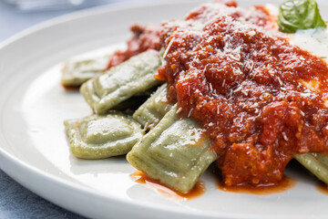 Spinach ravioli, served with bolognese sauce and béchamel sauce, served on a rustic plate, stacked on a gray rustic wooden backdrop.