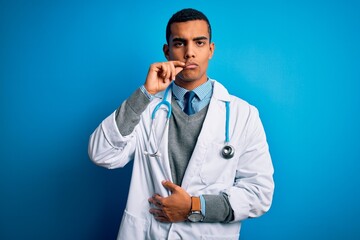Handsome african american doctor man wearing coat and stethoscope over blue background mouth and...