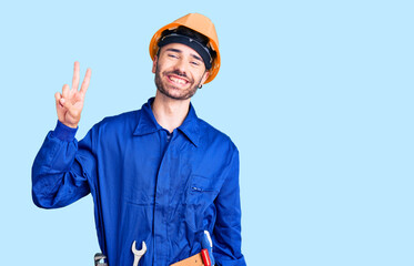 Young hispanic man wearing worker uniform smiling looking to the camera showing fingers doing victory sign. number two.