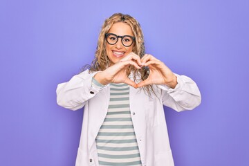 Young beautiful blonde scientist woman wearing coat and glasses over purple background smiling in love showing heart symbol and shape with hands. Romantic concept.