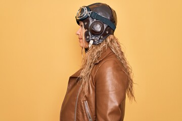 Young beautiful blonde aviator woman wearing vintage pilot helmet whit glasses and jacket looking to side, relax profile pose with natural face with confident smile. © Krakenimages.com