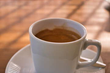 This unique photo shows a white cup with a saucer and inside it a hot cafe with a cream on top. The picture was taken from the side