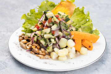 Vegetable ceviche with cucumber, onion, carrot, served with cancha serrana and crispy plantain, served in a white plate on a gray textured wooden background.