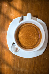 This unique photo shows a white cup with a saucer and inside it a hot cafe with a cream on top. The picture was taken from above