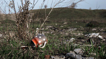 Garbage dump in the natural landscape. Red-white burnt kettle in the foreground, blurred background.