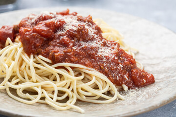 Close up of a spaghetti with Bolognese sauce and Parmesan cheese served on a stylish and textured light brown plate, isolated on a gray wooden textured background.