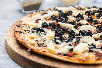 Pizza with black olives served on a rustic wooden board and set on a textured gray wooden background