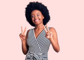 Young african american woman wearing casual clothes smiling looking to the camera showing fingers doing victory sign. number two.