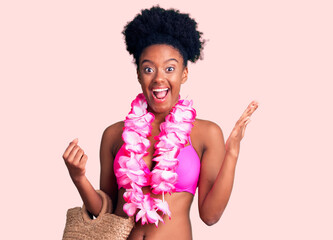 Young african american woman wearing bikini and hawaiian lei celebrating victory with happy smile...