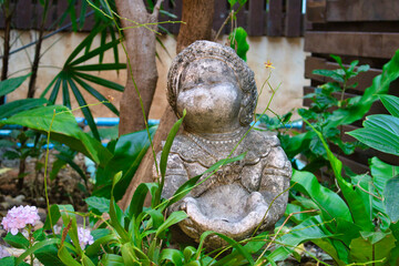 This unique photo shows an old weathered stone statue which is supposed to represent a fat woman. There are many leaves and a flower around the figure