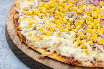 Close up of corn pizza served on a rustic wooden circular board, placed on a rustic gray wooden background.