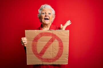 Senior beautiful grey-haired woman holding banner with prohibited signal over red background very...