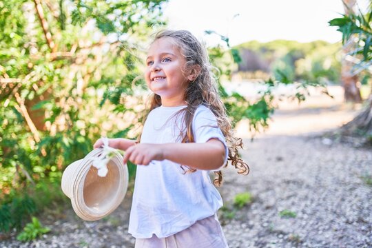 Adorable blonde child smiling happy holding summer hat. Walking and playing around the park