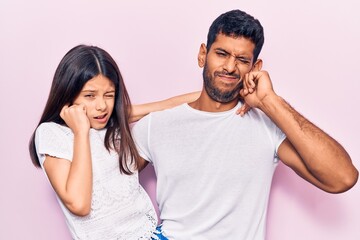 Young father and daughter wearing casual clothes covering ears with fingers with annoyed expression for the noise of loud music. deaf concept.