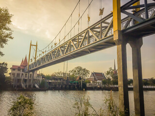 Small suspension steel bridge structure detail. Steel structure support of the suspension bridge across the river with sunset and blue sky background.
