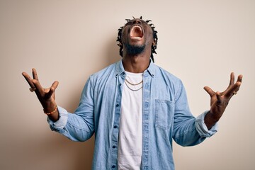 Fototapeta premium Young handsome african american man wearing casual denim shirt over white background crazy and mad shouting and yelling with aggressive expression and arms raised. Frustration concept.