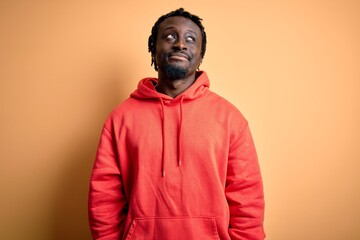 Fototapeta premium Young african american sporty man wearing sweatshirt with hoodie over yellow background looking away to side with smile on face, natural expression. Laughing confident.