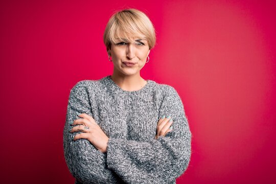 Young blonde woman with modern short hair wearing casual sweater over pink background skeptic and nervous, disapproving expression on face with crossed arms. Negative person.