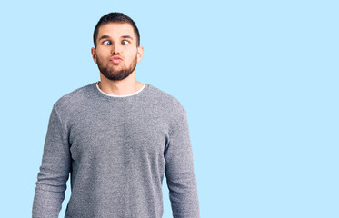 Young handsome man wearing casual sweater making fish face with lips, crazy and comical gesture. funny expression.