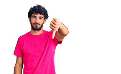 Handsome young man with curly hair and bear wearing casual pink tshirt looking unhappy and angry showing rejection and negative with thumbs down gesture. bad expression.