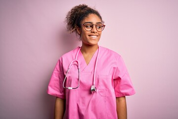 African american nurse girl wearing medical uniform and stethoscope over pink background looking...
