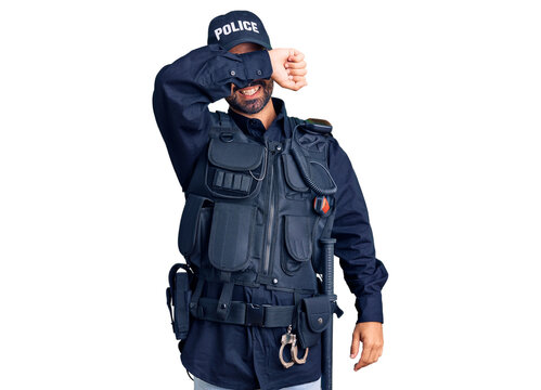 Young hispanic man wearing police uniform covering eyes with arm smiling cheerful and funny. blind concept.