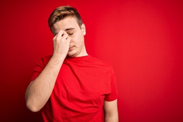 Young handsome redhead man wearing casual t-shirt over isolated red background tired rubbing nose...