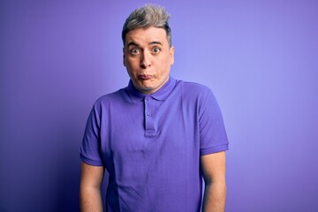 Obraz premium Young handsome modern man wearing casual purple t-shirt over isolated background puffing cheeks with funny face. Mouth inflated with air, crazy expression.