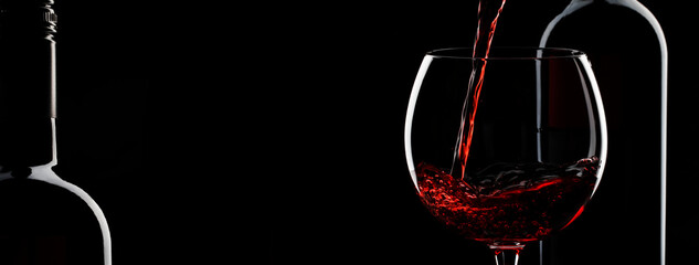 Fototapeta na wymiar Pouring red wine into the glass against black background. Panoramic banner with copy space