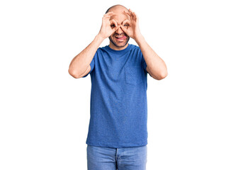 Young handsome man wearing casual t shirt doing ok gesture like binoculars sticking tongue out, eyes looking through fingers. crazy expression.