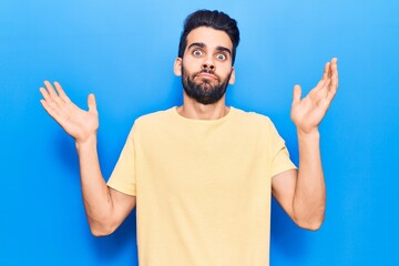 Young handsome man with beard wearing casual t-shirt clueless and confused with open arms, no idea...