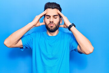 Young handsome man with beard wearing casual t-shirt with hand on head, headache because stress. suffering migraine.