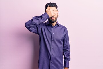 Fototapeta premium Young handsome man with beard wearing casual shirt covering eyes with hand, looking serious and sad. sightless, hiding and rejection concept