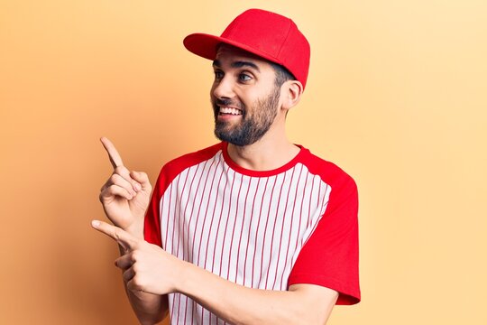 Young handsome man with beard wearing baseball cap and t-shirt smiling and looking at the camera pointing with two hands and fingers to the side.