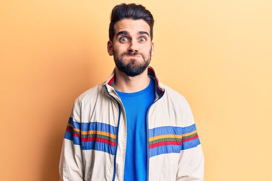 Young handsome man with beard wearing casual jacket puffing cheeks with funny face. mouth inflated with air, crazy expression.