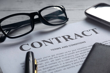 Selective focus of glasses,mobile phone,pen,notebook and Contract letter on a white wooden background.