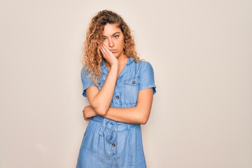 Young beautiful woman with blue eyes wearing casual denim dress over white background thinking looking tired and bored with depression problems with crossed arms.