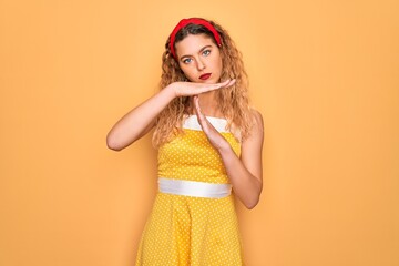 Beautiful blonde pin-up woman with blue eyes wearing diadem standing over yellow background Doing...