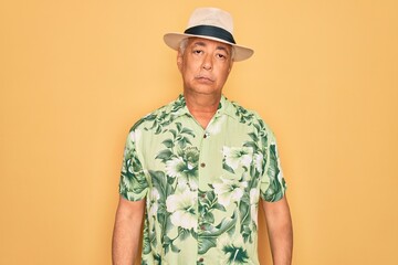 Middle age senior grey-haired man wearing summer hat and floral shirt on beach vacation Relaxed with serious expression on face. Simple and natural looking at the camera.