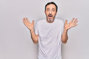 Middle age handsome man wearing casual t-shirt standing over isolated white background clueless and confused with open arms, no idea and doubtful face.