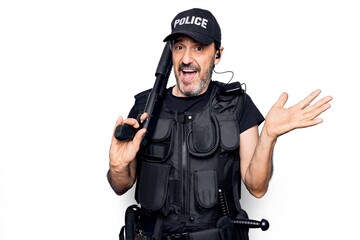 Middle age handsome policeman wearing police uniform and bulletproof vest holding shotgun celebrating achievement with happy smile and winner expression with raised hand